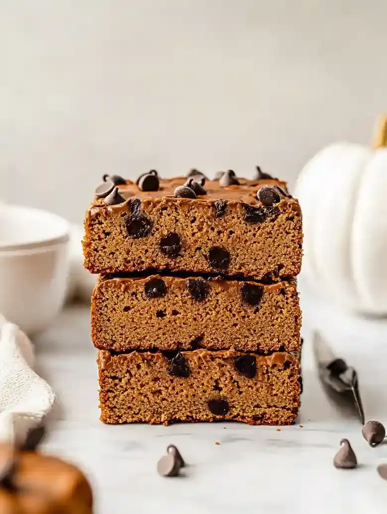 Stack of golden-brown pumpkin loaf slices with chocolate chips on marble.