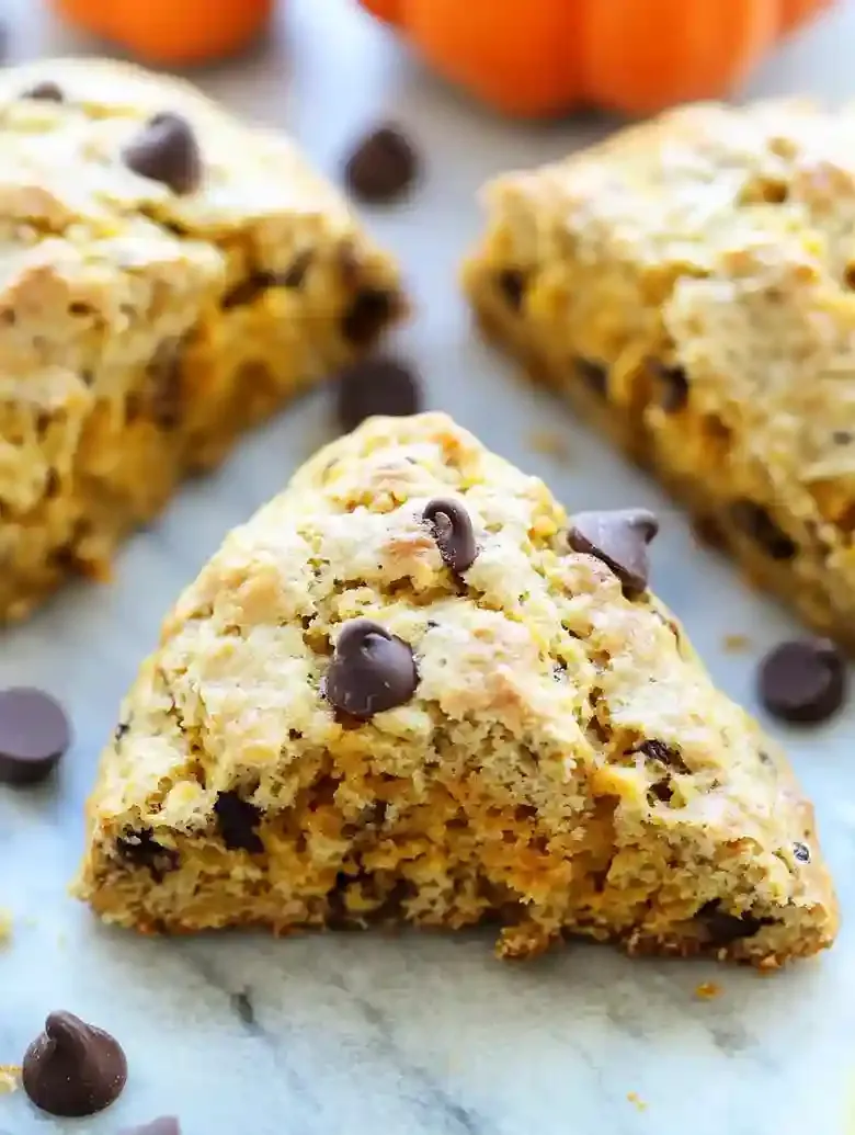 Freshly baked pumpkin scones with chocolate chips on marble surface.