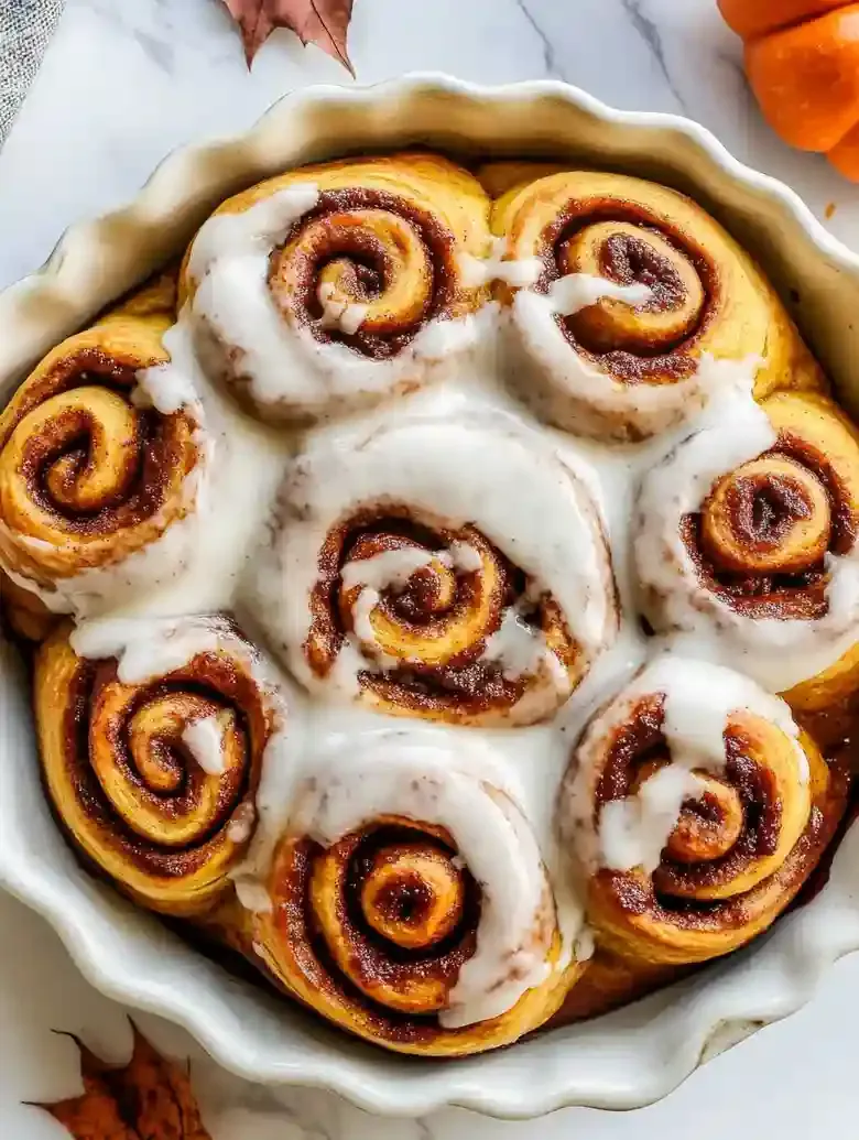 Pumpkin cinnamon rolls with cream cheese icing in a circular baking dish.