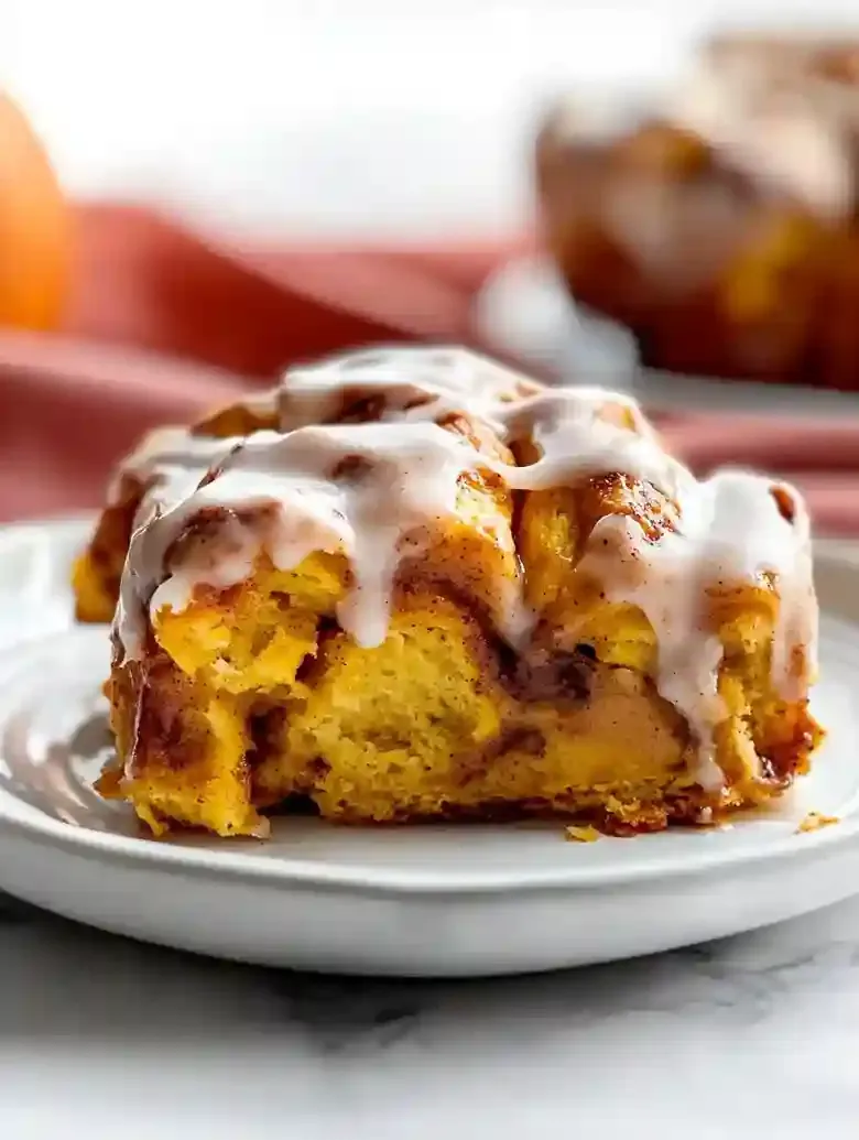 Pumpkin cinnamon roll on a plate, drizzled with cream cheese icing.