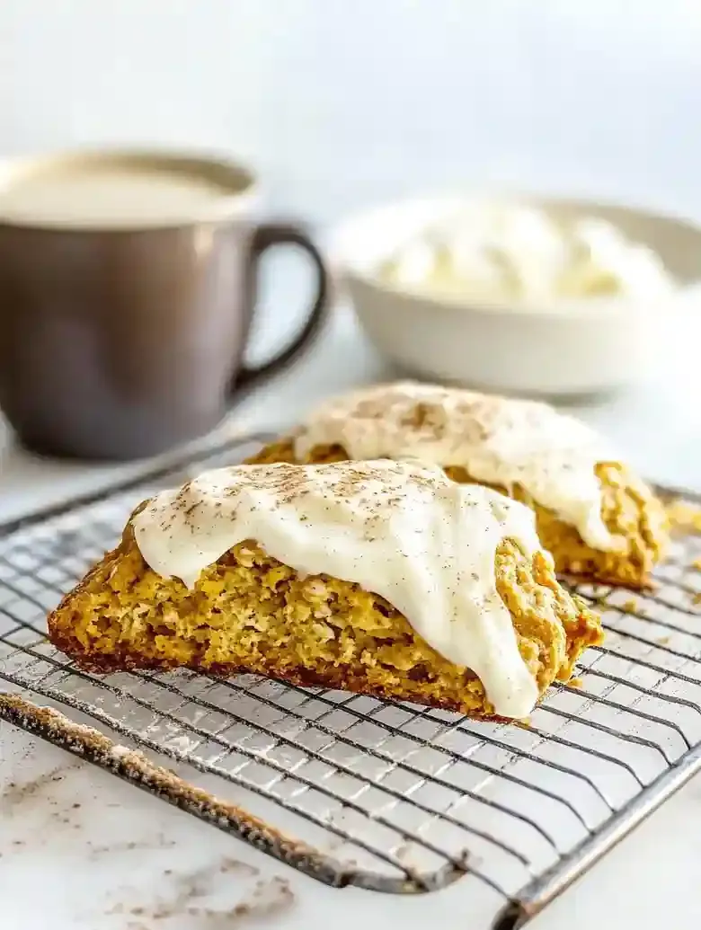 Pumpkin cream cheese scone with icing and cinnamon on a marble surface.