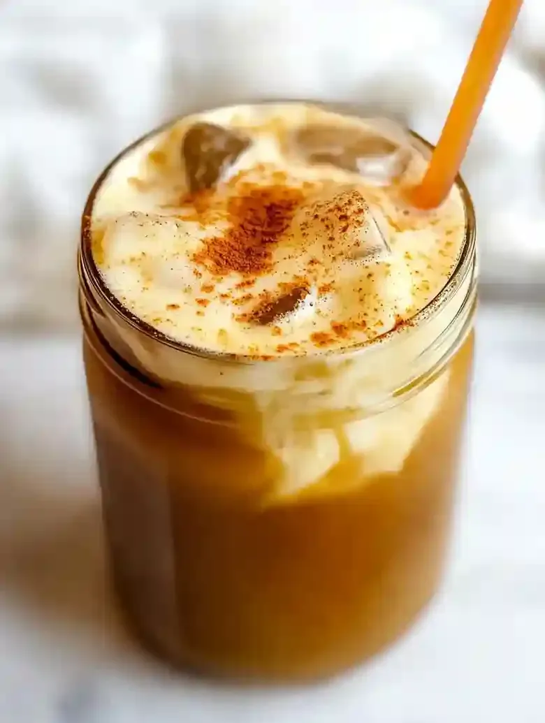 Iced coffee in a glass jar topped with pumpkin cold foam and spice.