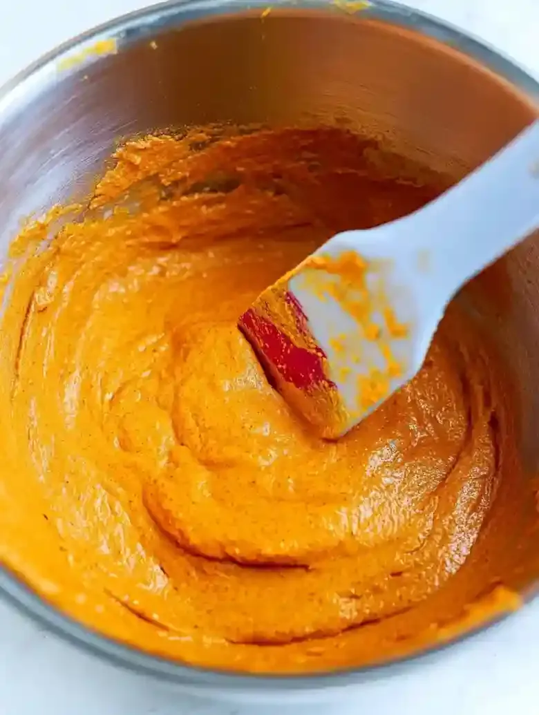 Stainless steel bowl with vibrant orange pumpkin batter and rubber spatula.