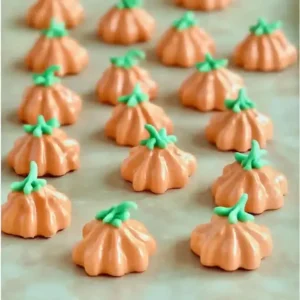 Meringue cookies shaped like pumpkins with green stems on marble surface.