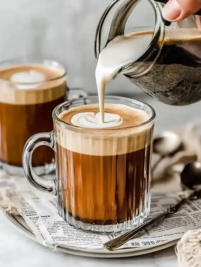 Glass mug of pumpkin spice latte with oat milk being poured, marble surface.
