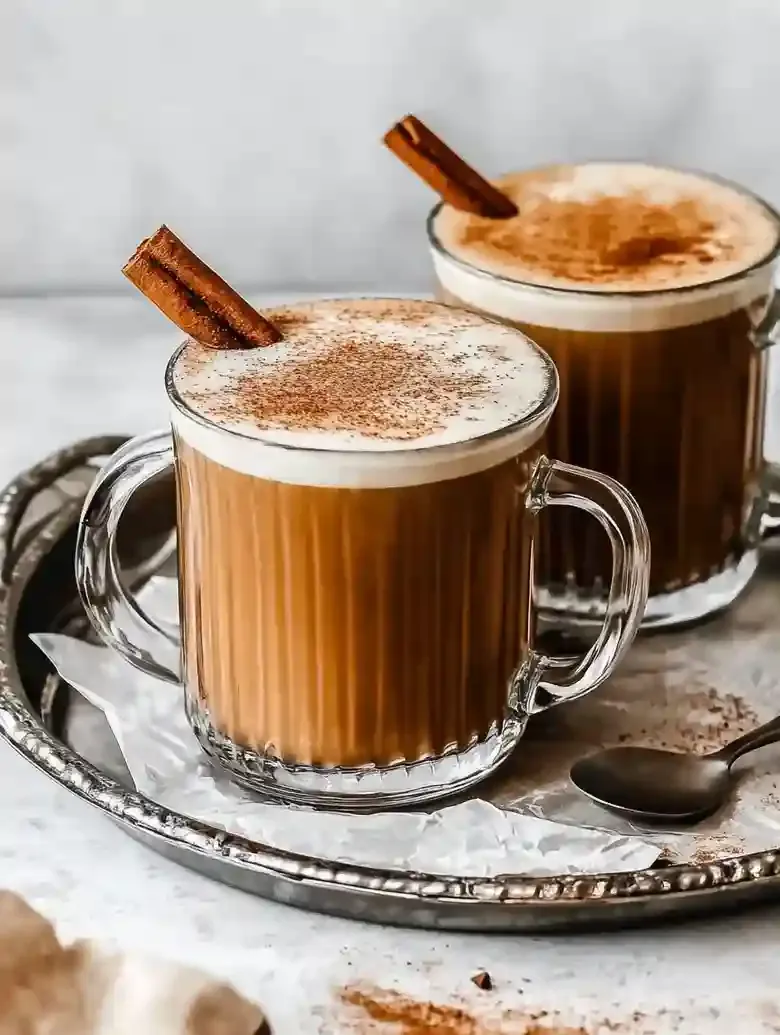 Two glass mugs with pumpkin-colored lattes on a silver tray.