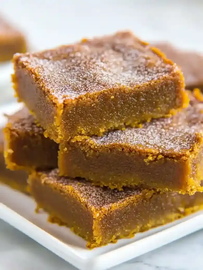Four stacked pumpkin snickerdoodle blondies on a white plate, one with a bite taken.