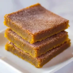 Three stacked pumpkin snickerdoodle blondies dusted with cinnamon and sugar.