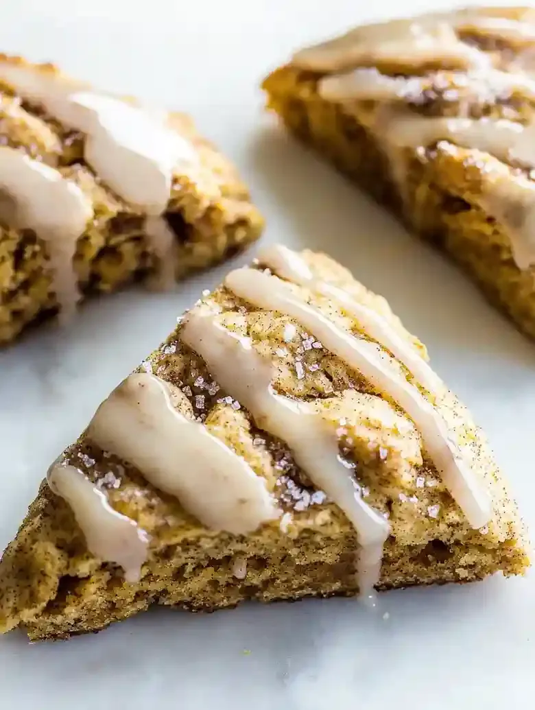 Three golden-brown pumpkin snickerdoodle scones with maple glaze on marble.