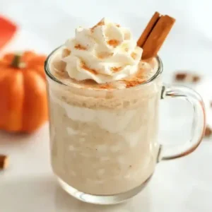 Closeup of glass mug with beverage, whipped cream, and cinnamon stick.