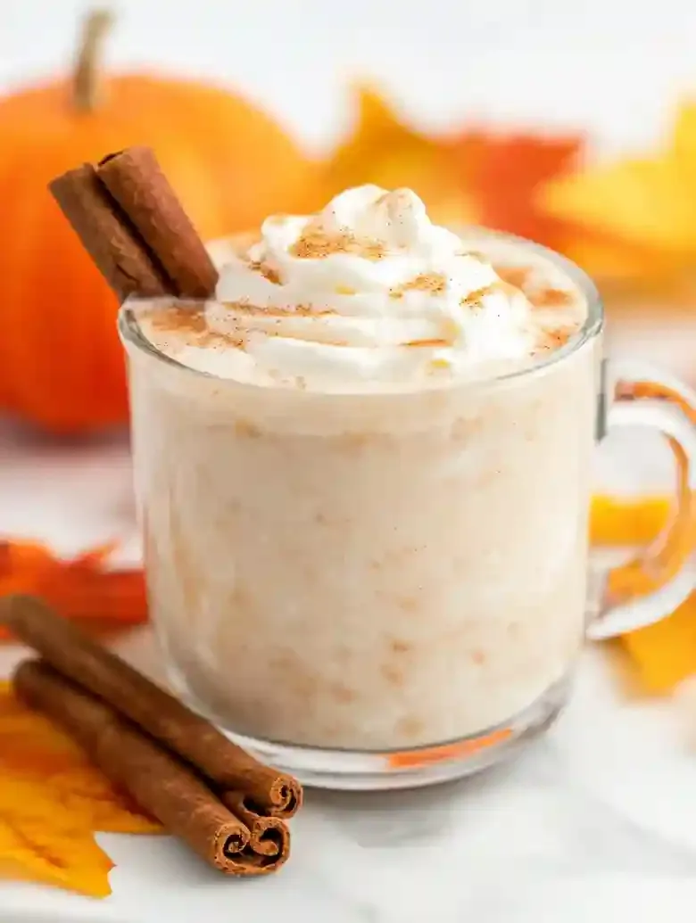 Glass mug filled with a light beverage, topped with whipped cream and spice.