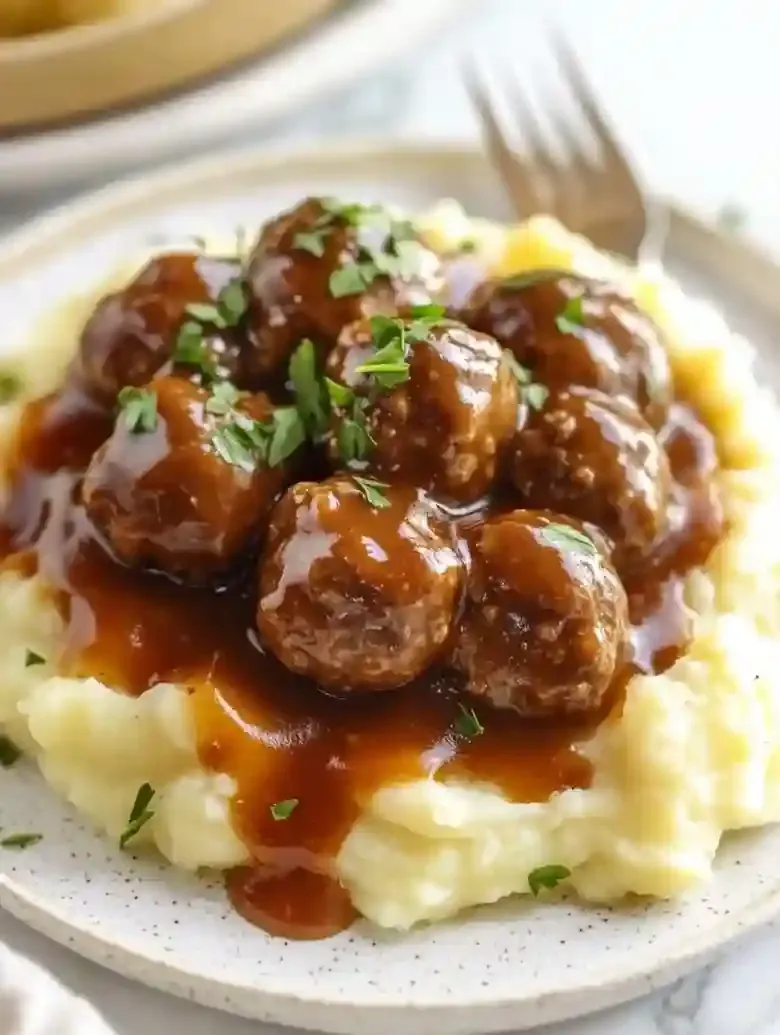 Salisbury steak meatballs on mashed potatoes with brown gravy and parsley.