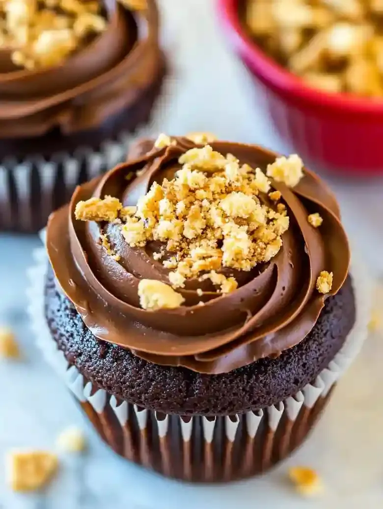 Chocolate cupcake with frosting and cookie crumbles on marble surface.