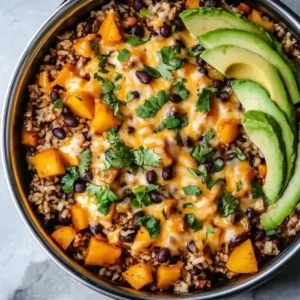 Skillet of potatoes, black beans, and rice topped with cheese and avocado.