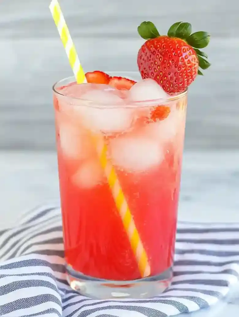 Tall glass with vibrant drink, ice, and fresh strawberries on marble.