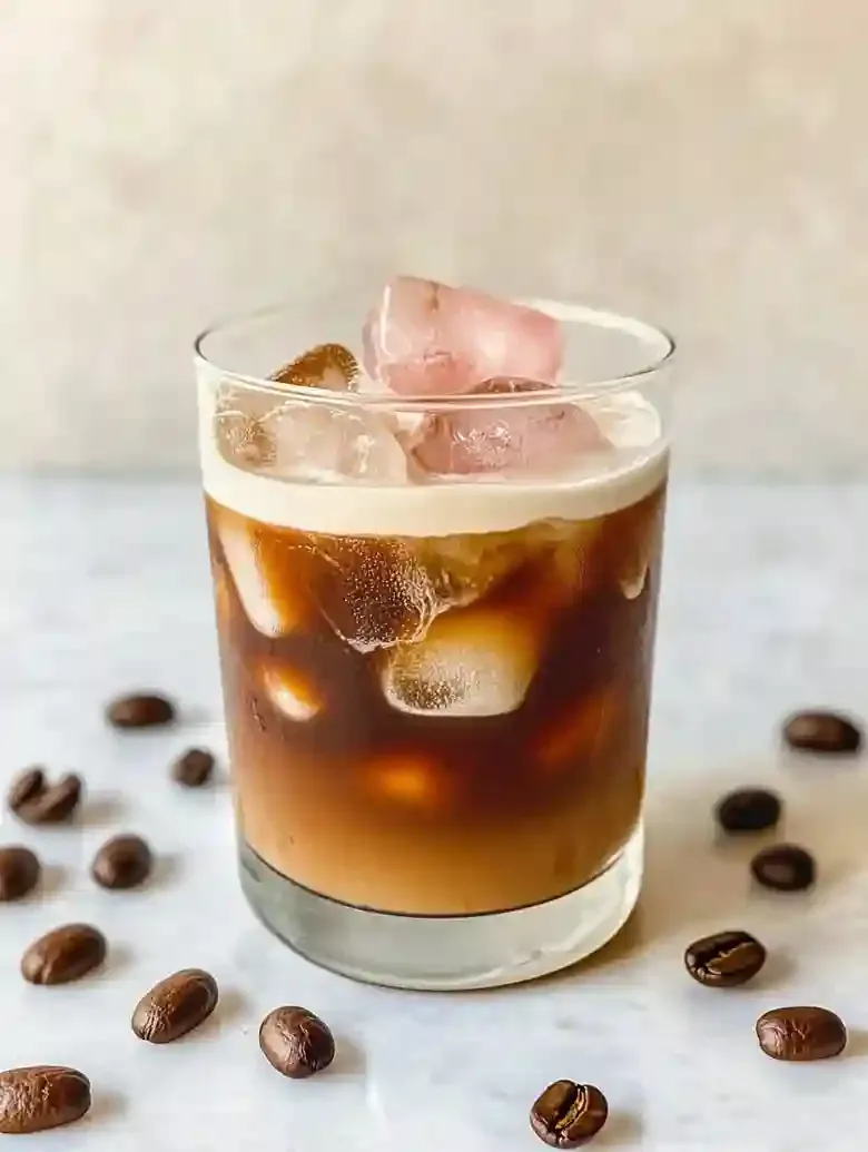 Layered coffee and cream drink with ice cubes on marble surface.
