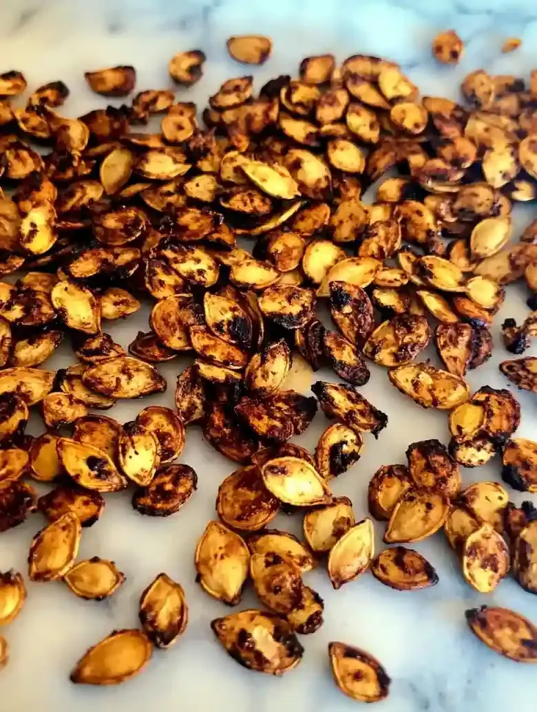 Roasted pumpkin seeds scattered on a white marble surface.