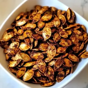 Closeup of roasted pumpkin seeds in a white bowl on marble.