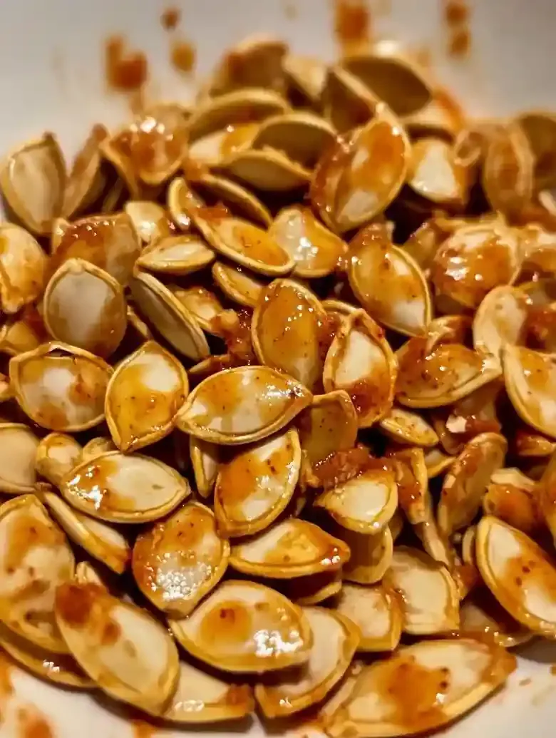 Closeup of reddish-orange seasoned pumpkin seeds on white marble.
