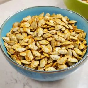 Blue bowl on marble surface filled with golden-brown curry pumpkin seeds.
