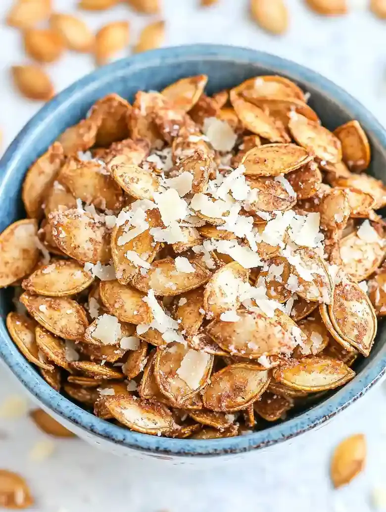 Bowl of garlic Parmesan pumpkin seeds on a marble surface, with extras.