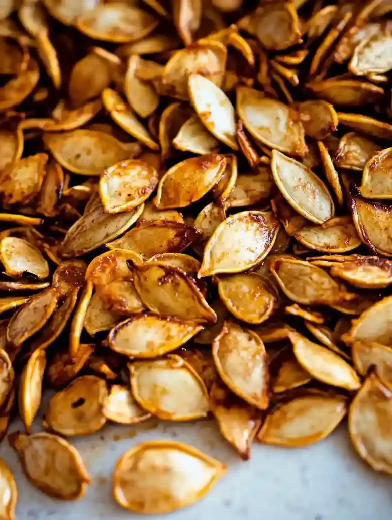 Roasted pumpkin seeds in various golden-brown hues on marble surface.