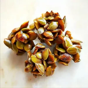 Clusters of shiny, golden-brown pumpkin seeds on white marble.