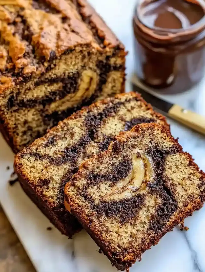 Banana bread with Nutella swirls on marble surface with knife and jar.